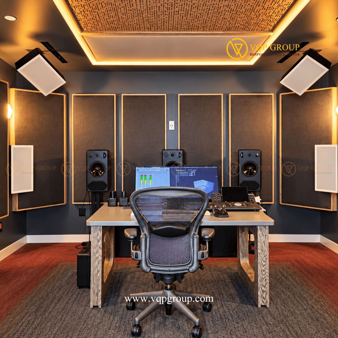 Phòng điều khiển âm thanh AMBER STUDIO với bàn làm việc và hệ thống loa kiểm âm Mô tả ảnh: Hình ảnh chính diện khu vực làm việc trung tâm của AMBER STUDIO, nổi bật với màn hình điều khiển, ba loa phía trước, tấm tiêu âm khung gỗ và hệ chiếu sáng trần.